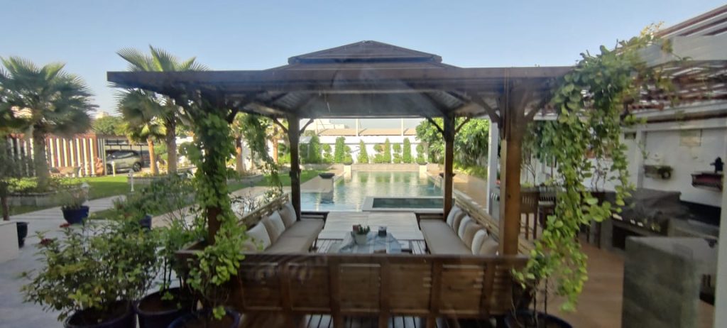 Picture looking through the covered seating area. Looking for a lush garden film location in Dubai? With real lawns, palm trees, bougainvillea, and a grand porch entrance, this villa garden is shoot-ready.